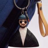 A hand-carved Léon movie keychain attached to a blue bag, featuring his iconic sunglasses, hat, and black jacket.